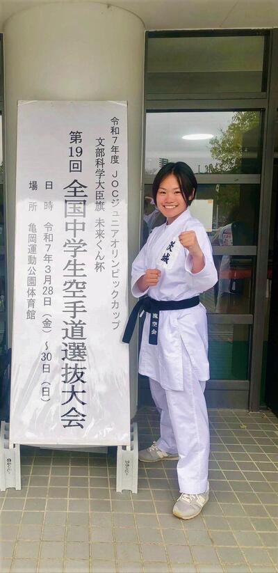 大会看板の横で空手のポーズを決めている石塚選手